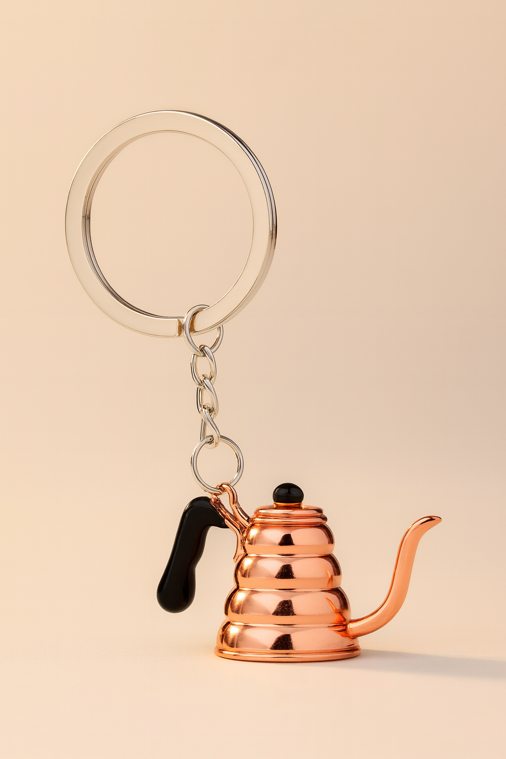 Copper-colored kettle keychain on a beige background